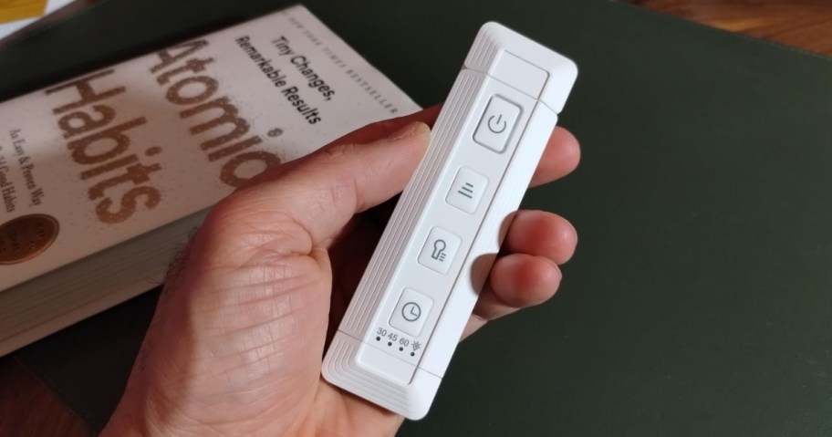 hand holding a white clip on rechargeable booklight with time, book in the background