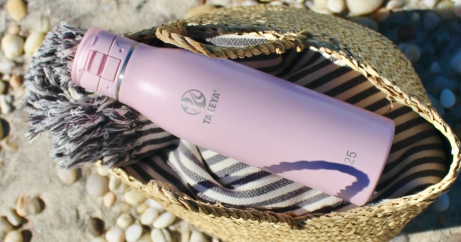 light pink Takeya travel coffee mug bottle in a woven straw beach bag on the beach