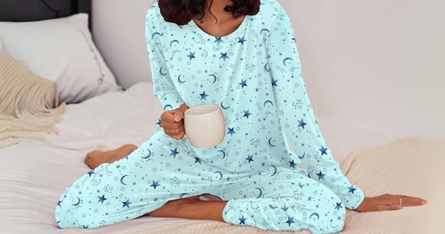 woman sitting on a bed with a coffee cup in her hand wearing a pair of light blue pajamas with dark blue moons and stars on them