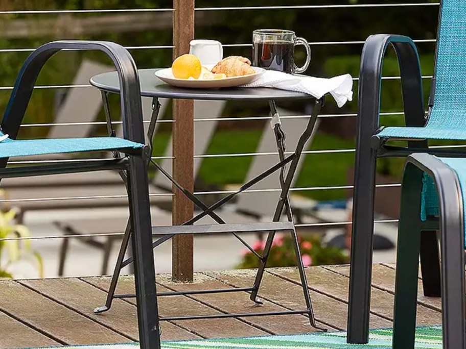 a small round patio table with food and coffee mug on it, next to 2 patio chairs