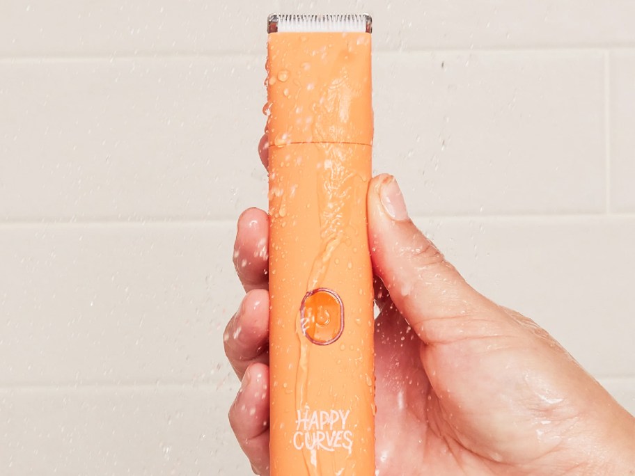 hand holding an orange bikini trimmer in shower under water