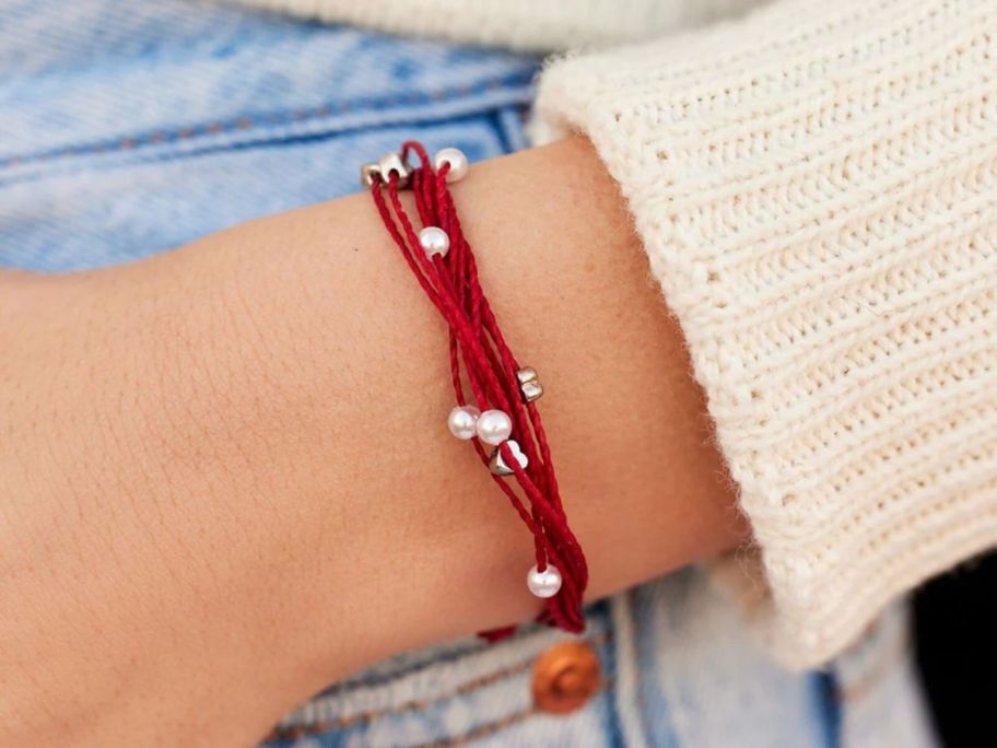 a womans wrist shown wearing a red multistring bracelet 