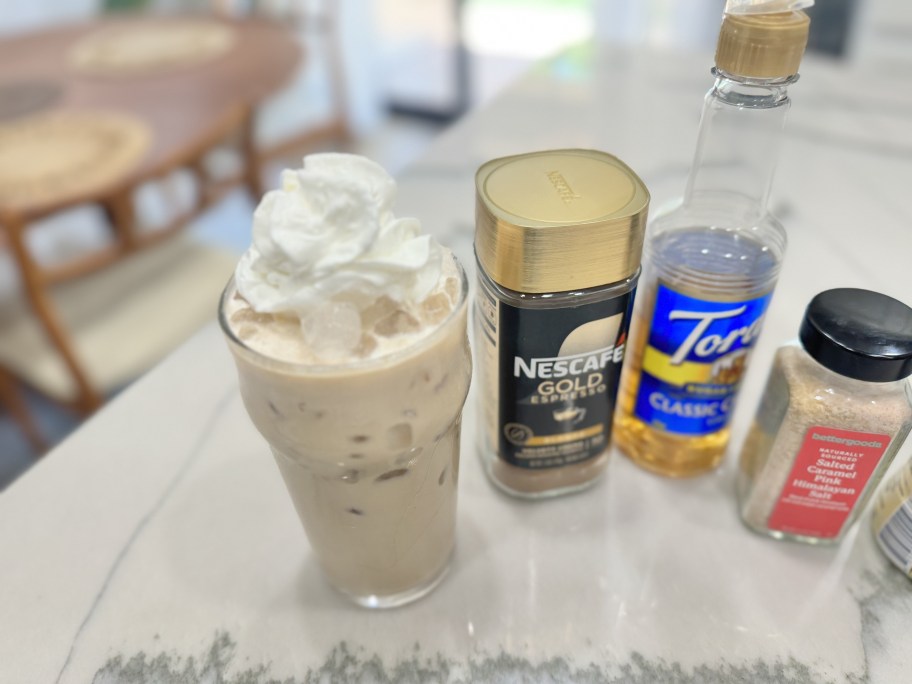 a coffee drink with whipped cream sitting on counter with NESCAFE coffee, Torani syrup, and caramel salt