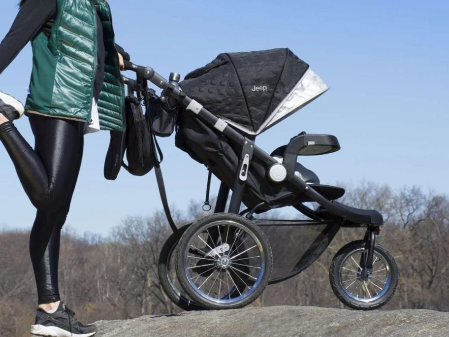 A woman standing on a large rock with a jogging stroller 