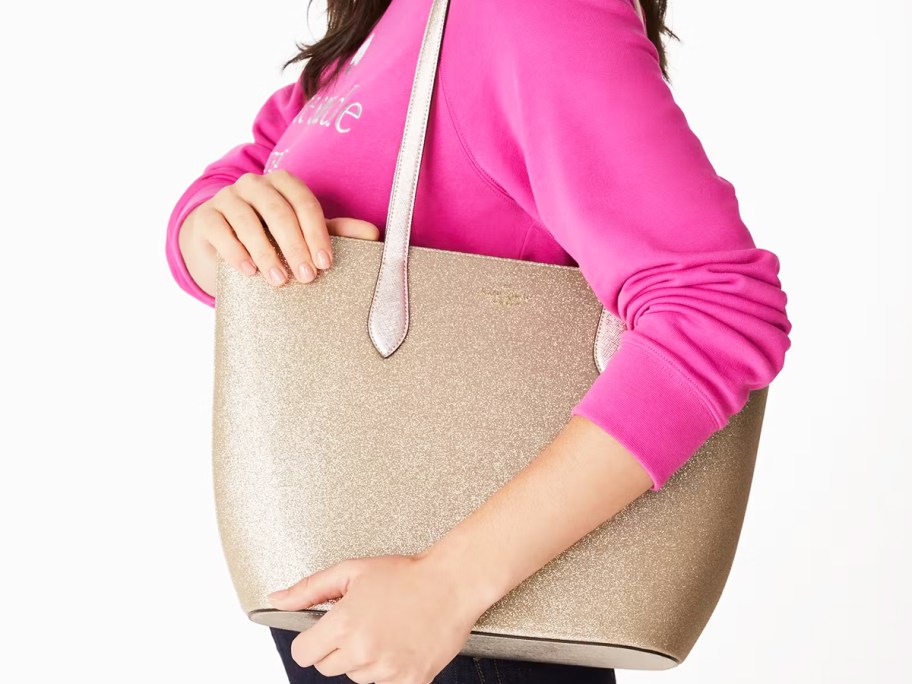 woman in a pink sweatshirt with a glittery gold tote bag