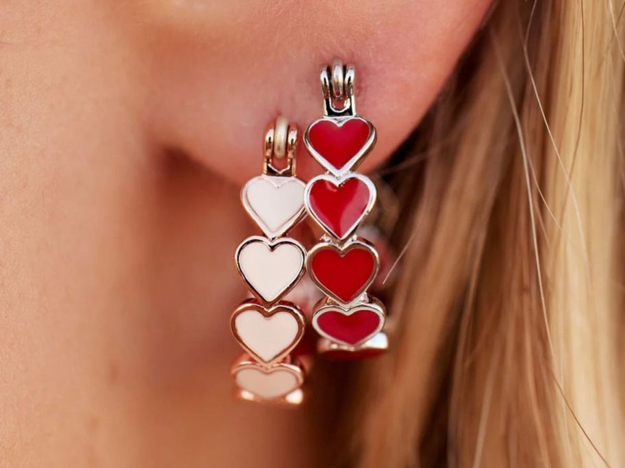 a womans ear lobe with two heart hoop earrings in silver and rose gold finishes