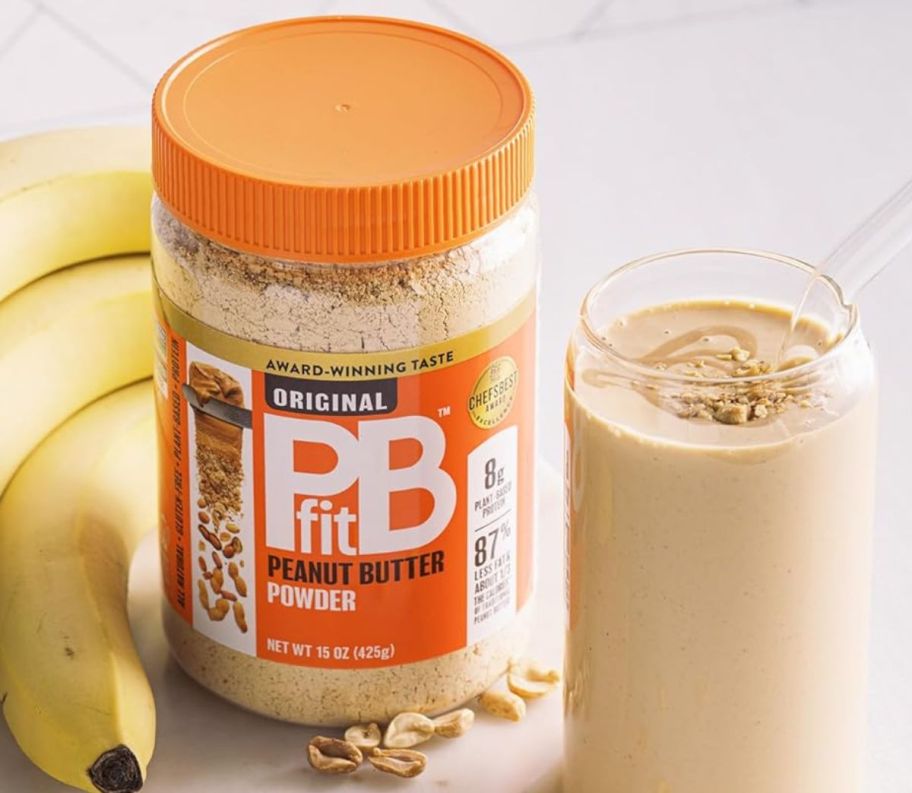 a 15oz jar of pb fit peanut butter powder next to bananas and a smoothie