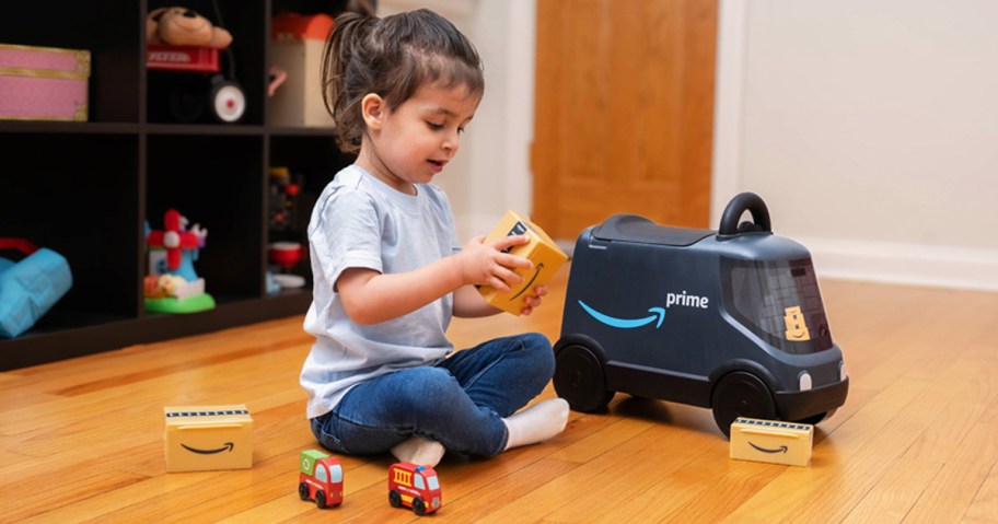 child sitting on floor next to a Radio Flyer Amazon Delivery Van ride-on toy