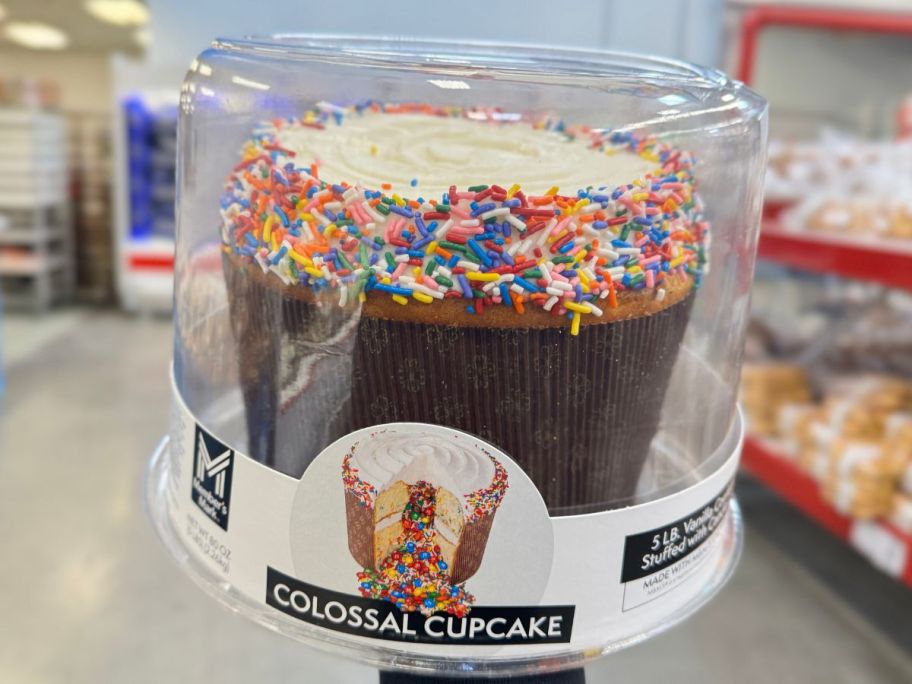 hand holding a giant cupcake covered in sprinkles in a plastic container at Sam's Club Bakery