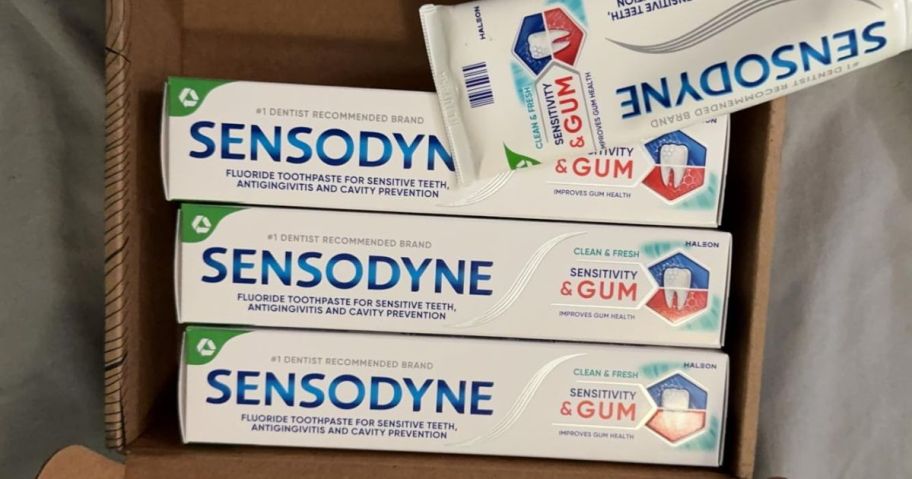 3 boxes of Sensodyne Sensitivity & Gum Toothpaste with one tube at the top in an open cardboard box