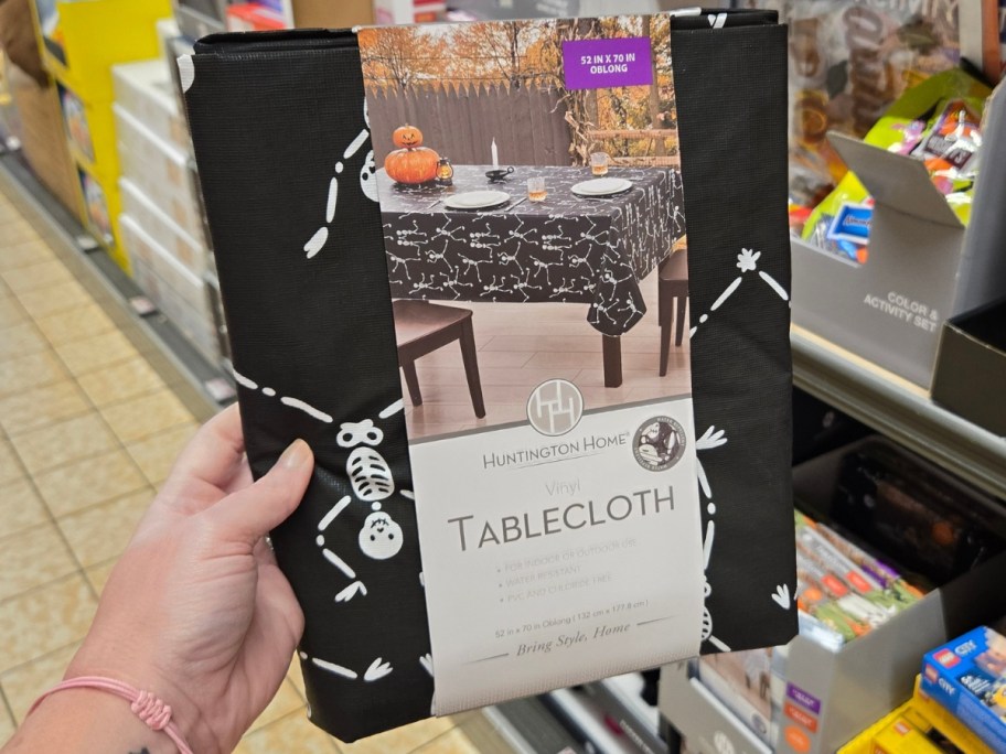 hand holding a black Halloween tablecloth with skeletons on it