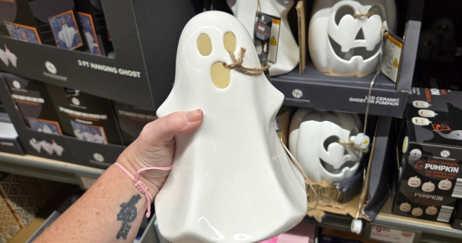 hand holding a white light up ceramic ghost Halloween decor piece, more ghosts and pumpkins in the background