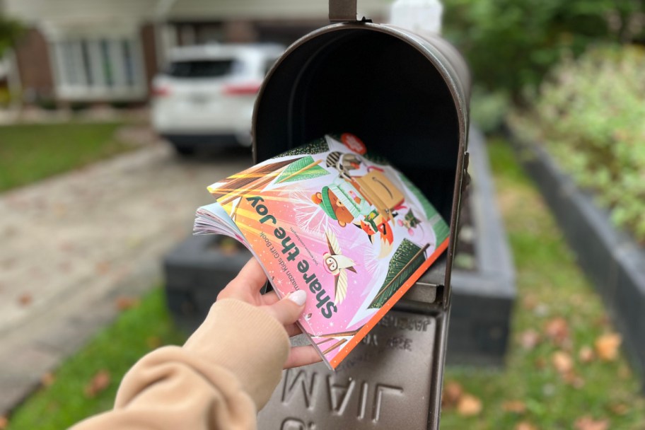 woman's hand pulling an amazon toy catalog out of a black mailbox