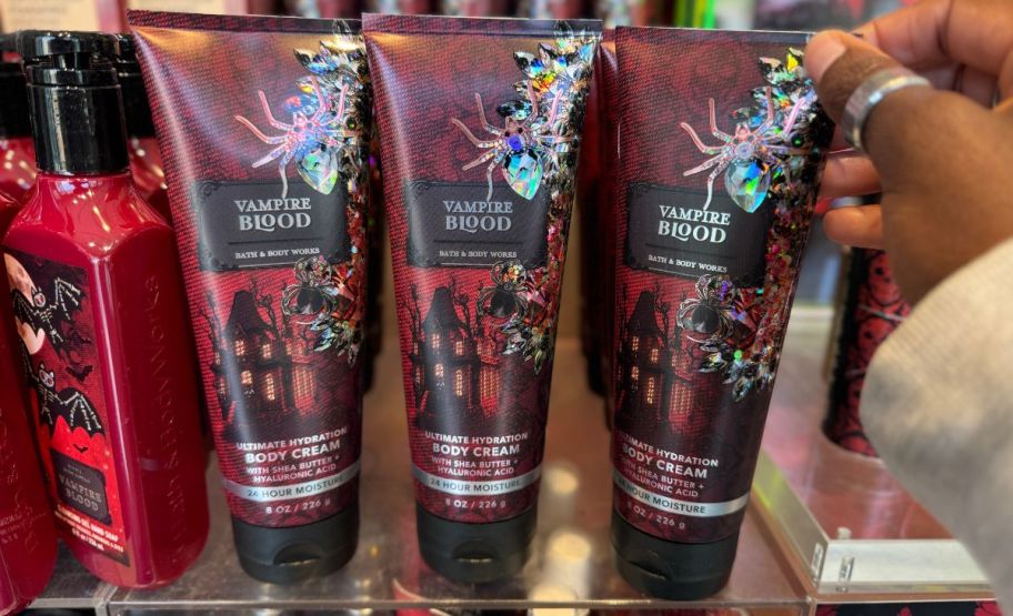 a woman hand grabbing a tube of vampire blood scented halloween body cream from a store display