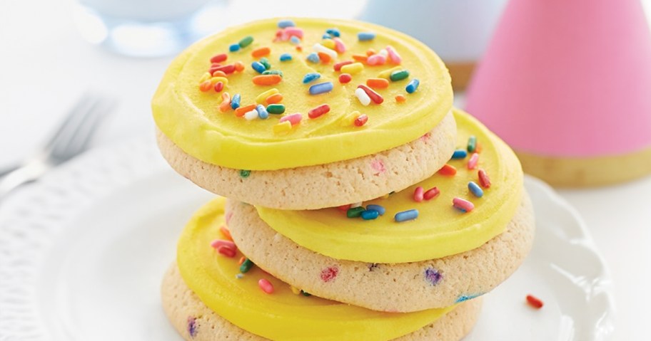 yellow iced cookies with sprinkles stacked on plate