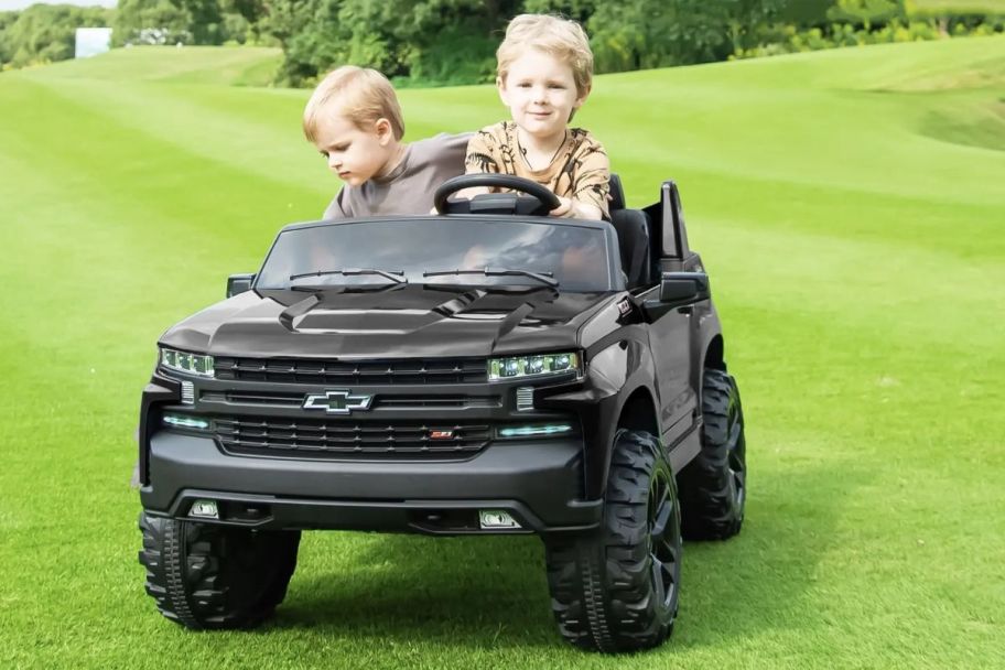 two kids riding on chevrolet electric ride on car on grass