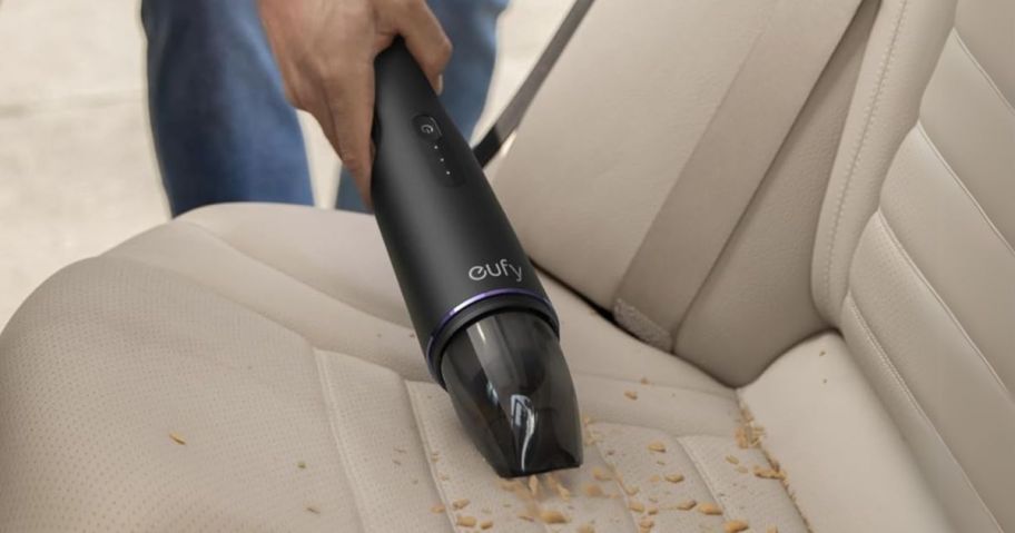 person using a cordless handheld vacuum to clean a mess from the seat of a car