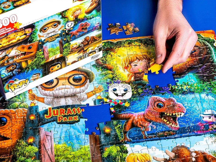 hand putting pieces of jurrasic park puzzle together with box laying next to it