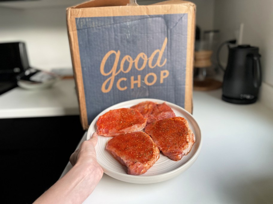 woman holding a plate of pork chops in front of a good chop box