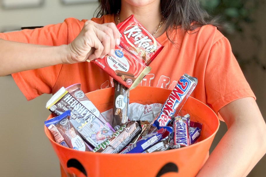 woman holding kitkat and great value candy bar over bowl