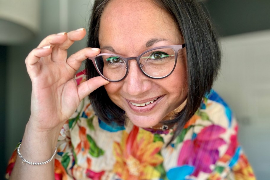 smiling woman wearing glasses, with her fingers holding the frame around one lens