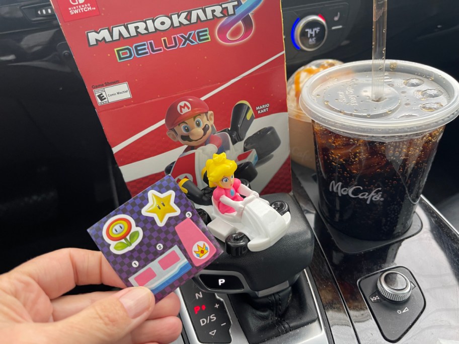 hand holding a mcdonalds mariokart toy in front of a happy meal box and soda in a car