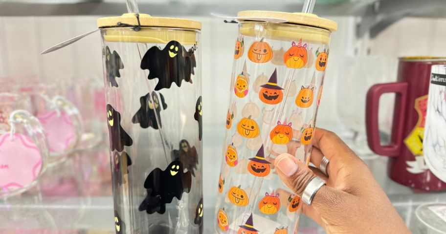 hand reaching for a tall glass tumbler with Jackolanterns on it, next to one with bats