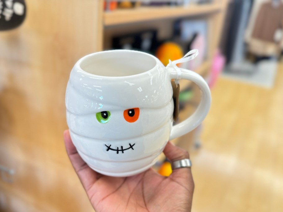 hand holding a coffee mug that looks like a mummy