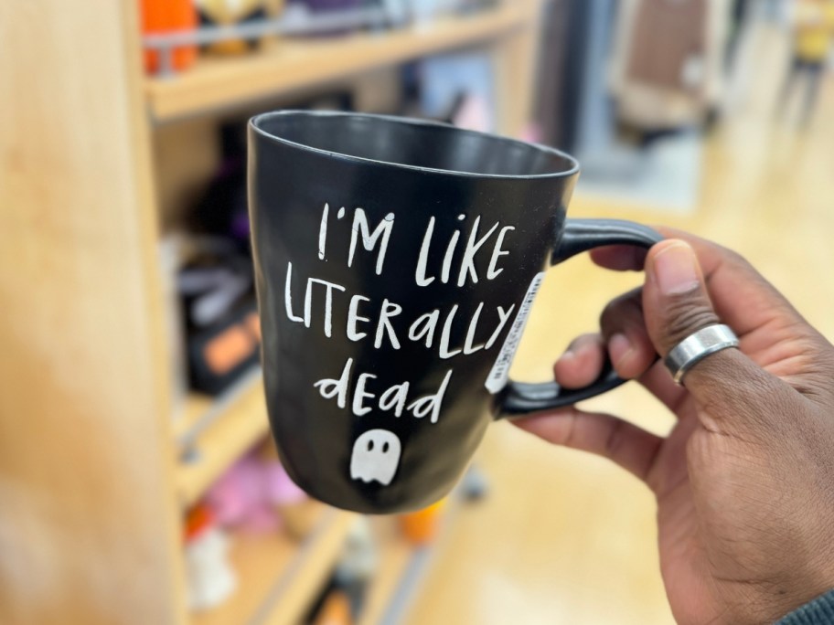 hand holding a black coffee mug with a ghost on it that says "I'm like literally dead"