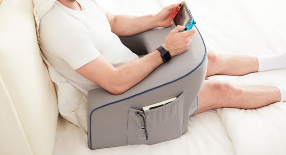 man sitting on bed with gray reading pillow playing on nintendo switch