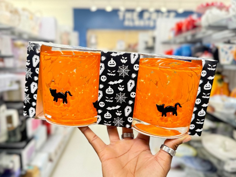 hand holding a set of orange marbled glass mugs with black cats on them