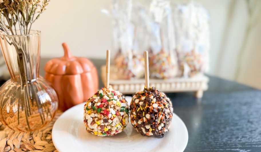 mrs prindables fall caramel apples displayed on a plate in front of more decorated apples in packaging, surrounded by fall decor