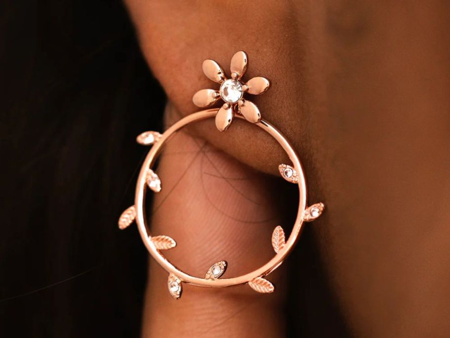 An ear lobe shown with a flower motif hoop earring. 