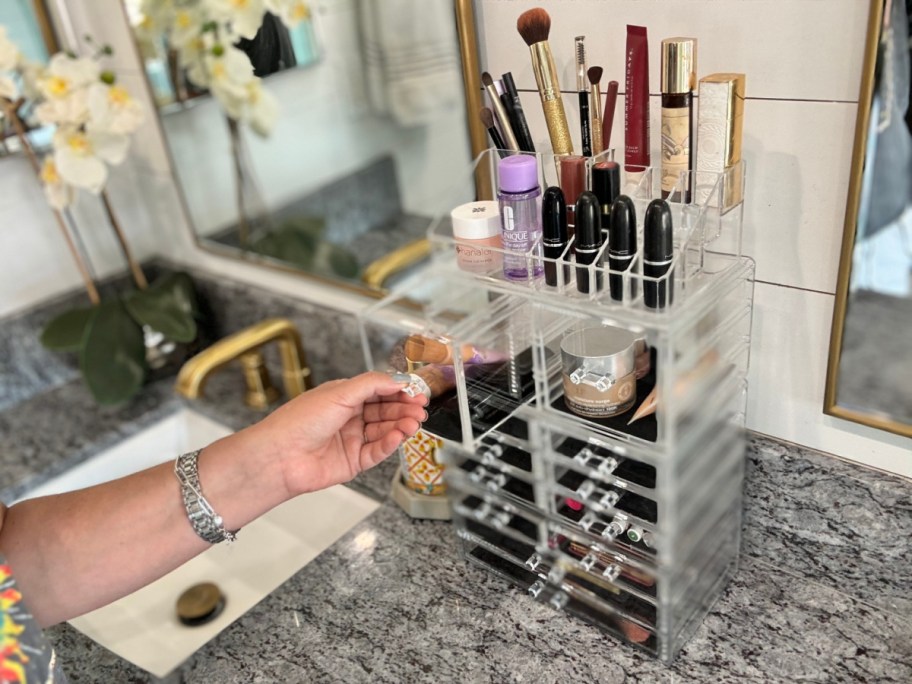 hand opening the drawer of a sorbus makeup organizer that is sitting on a bathroom counter, filled with makeup