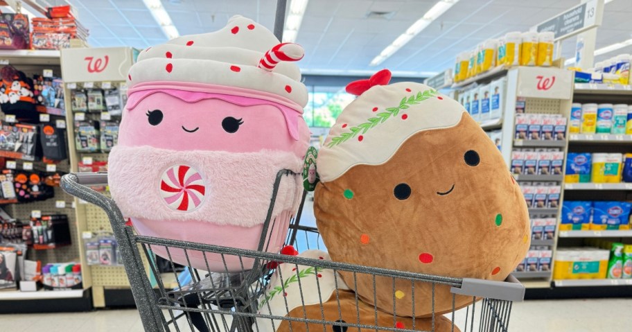 two large Squishmallows in a Walgreens cart in the middle of the store - one is a pink hot chocolate and the other is fruitcake