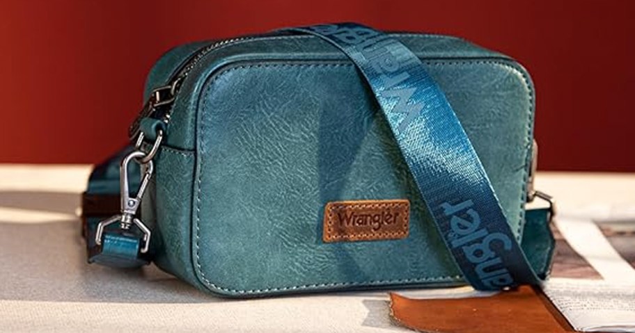 teal crossbody wrangler bag on table