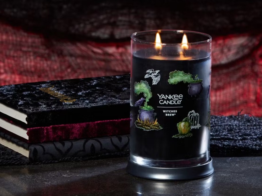 black Yankee Candle Large Signature Jar Candle lit with Witches Brew scent, next to some old books