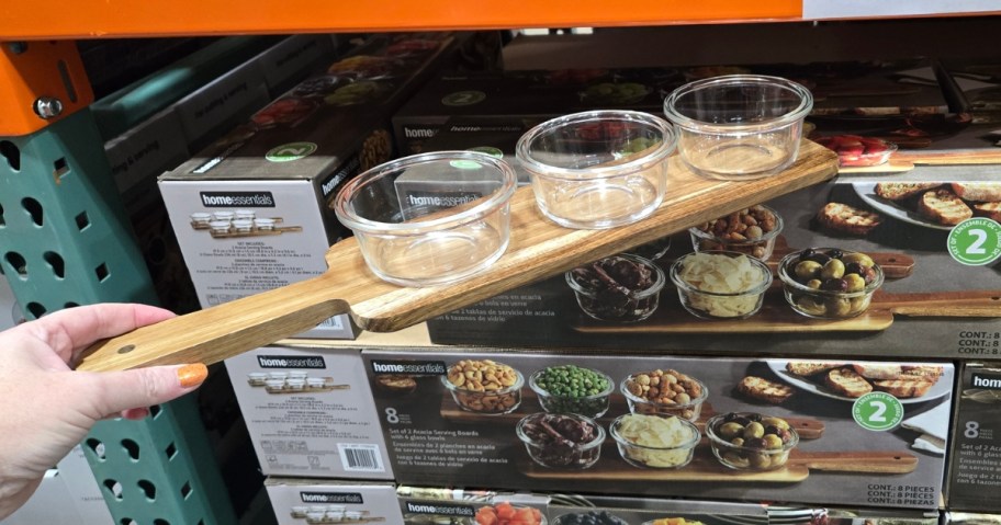 hand holding a wooden serving board with 3 glass bowls, boxes of them behind it on a Costco shelf