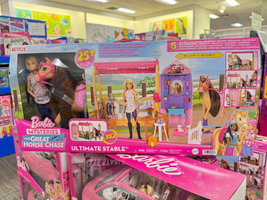 a box with a Barbie Mysteries: The Great Horse Chase Stable 25-Piece Set in it stacked on top of more in store