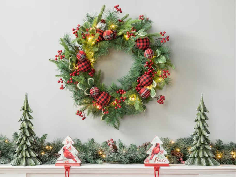 a large Christmas wreath above a fireplace mantle with more Christmas decor on it