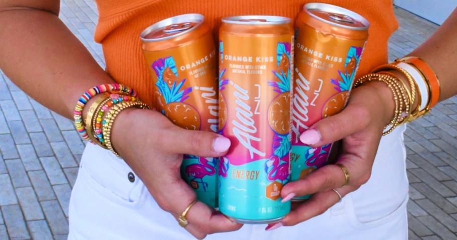 woman holding 2 cans of Alani Energy Drinks Orange Kiss