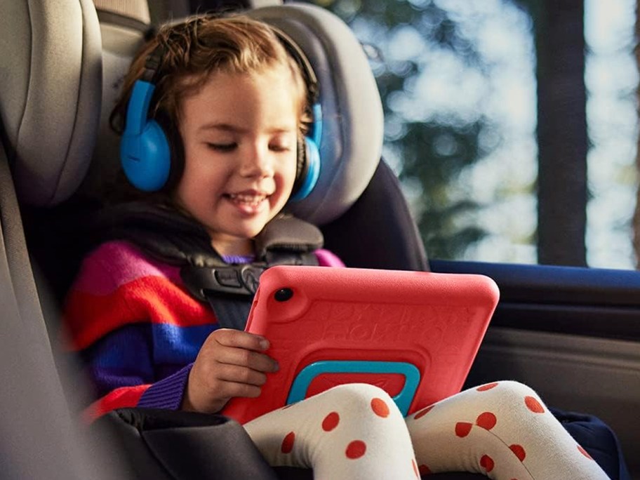 girl in car seat holding a red fire kids tablet