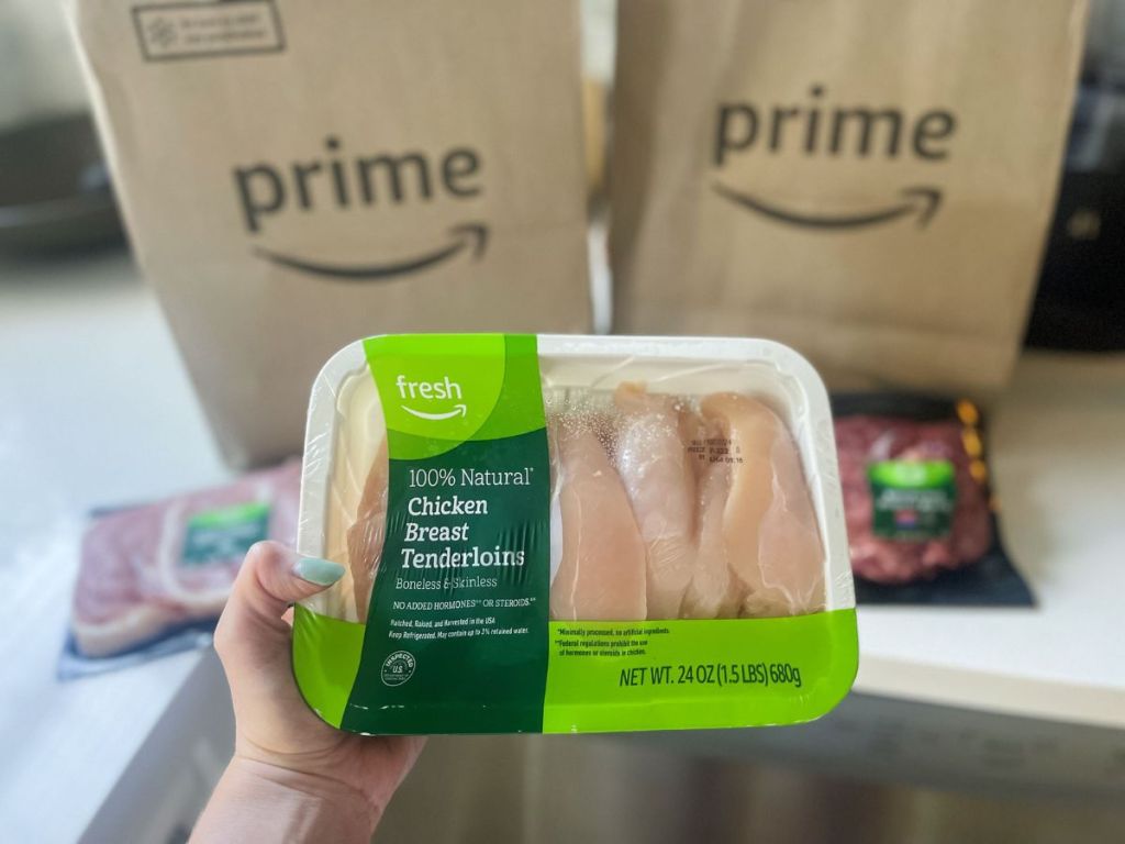 Amazon Prime bags in the background as a person holds a package of raw chicken