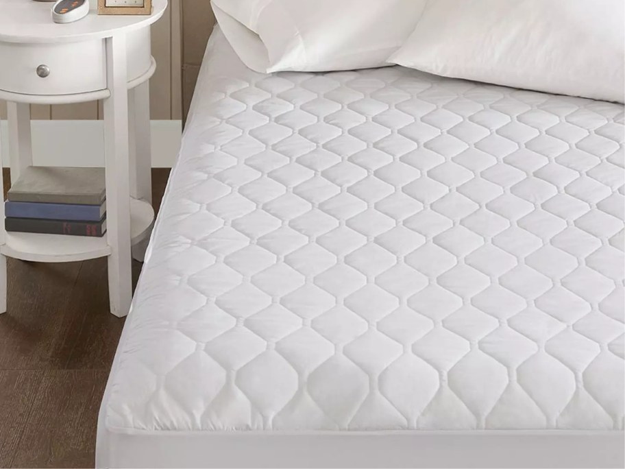 a bed with a white mattress top and two white pillows on it next to a nightstand