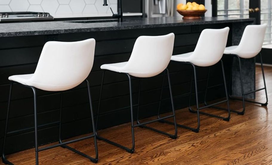 4 white counter height bar stools pulled up to a bar counter in a kitchen