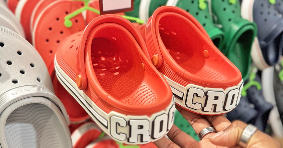 hand holding up a pair of red and white crocs clogs that say CROCS on the back