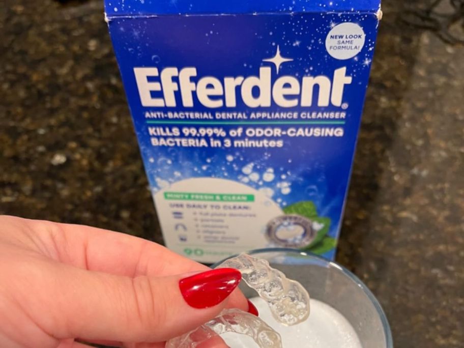 A person holding retainers near a box of Efferdent Cleaning Tablet 44-Count (Minty Fresh & Clean)