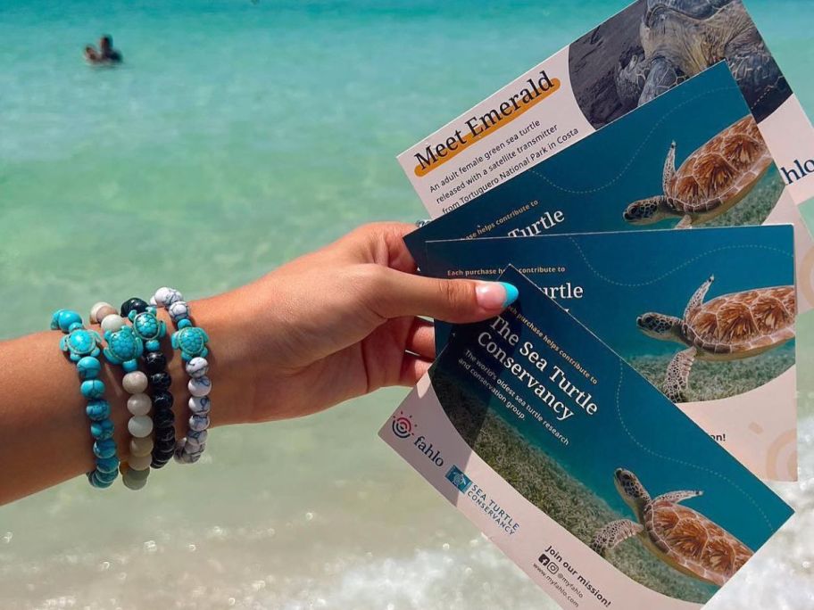 Woman holding Sea Turle tracking cards whil;e wearing 3 Fahlo animal tracking bracelets