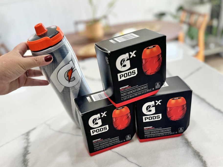 hand touching bottle near 3 stacked boxes of Gatorade Gx Pods