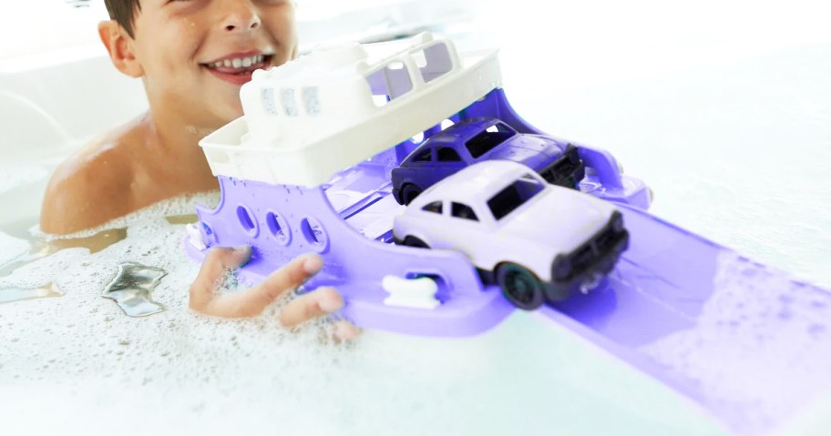 boy playing with purple ferry boat toy in bathtub